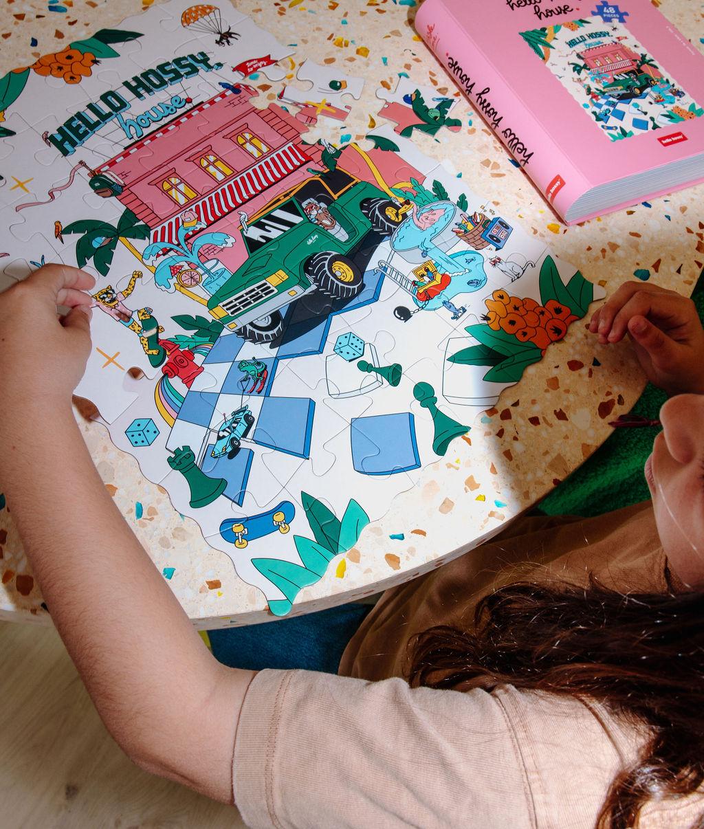 Fille assemblant le puzzle coloré 48 pièces "Hello Hossy House" sur une table – vue du dessus – Hello Hossy