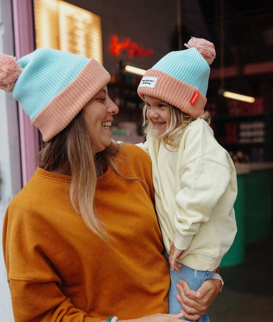 Bonnet avec pompon Color Block Candy porté par une mère avec sa fille dans les bras – photo lifestyle – Hello Hossy